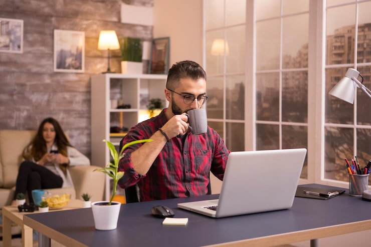 bearded-caucasian-entrepreneur-taking-sip-coffee-while-working-laptop-living-room-girlfriend-sofa-background-browsing-phone-chips-table_482257-31207