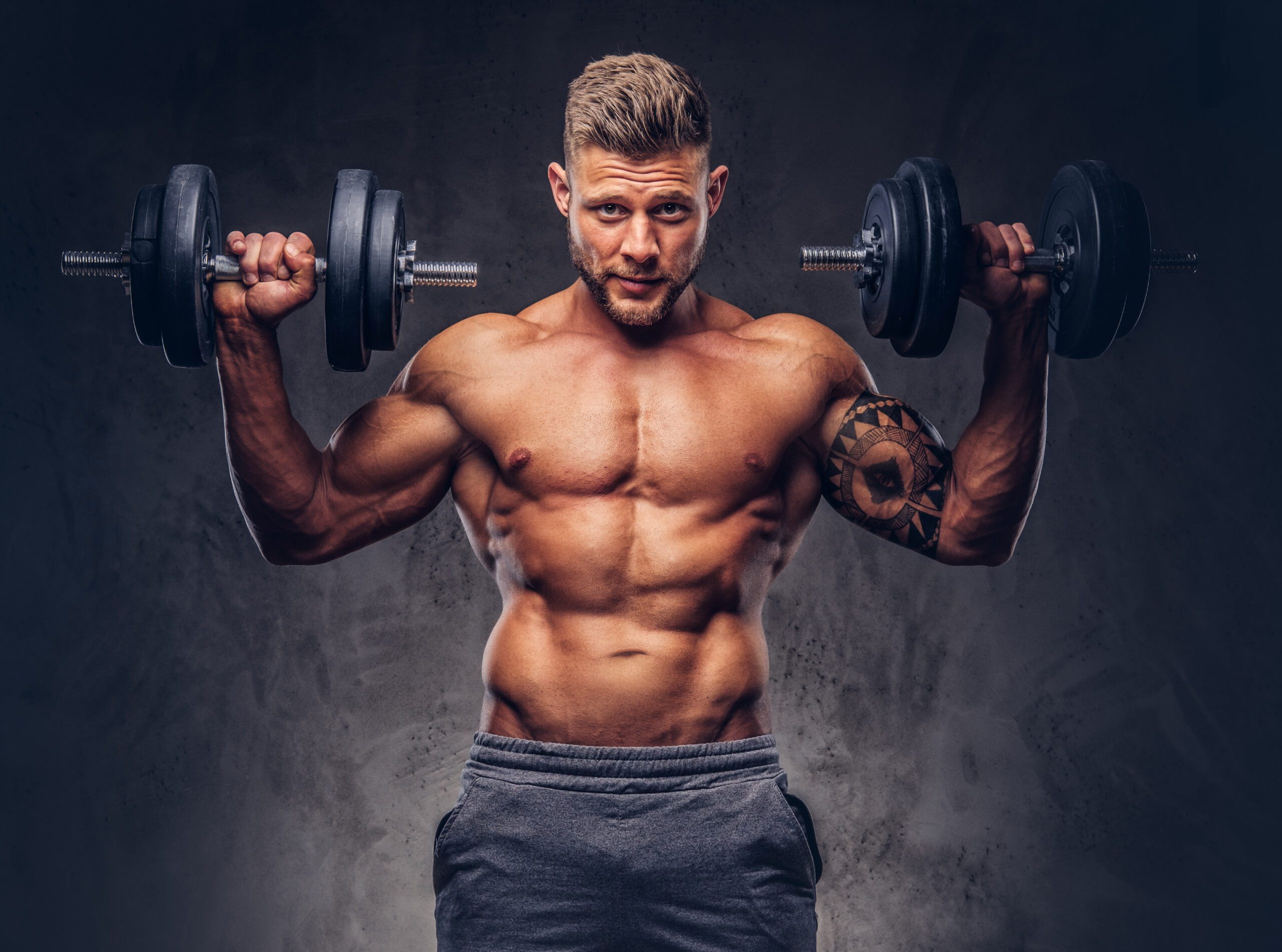 Handsome shirtless tattooed bodybuilder wearing sports shorts, posing in a studio.